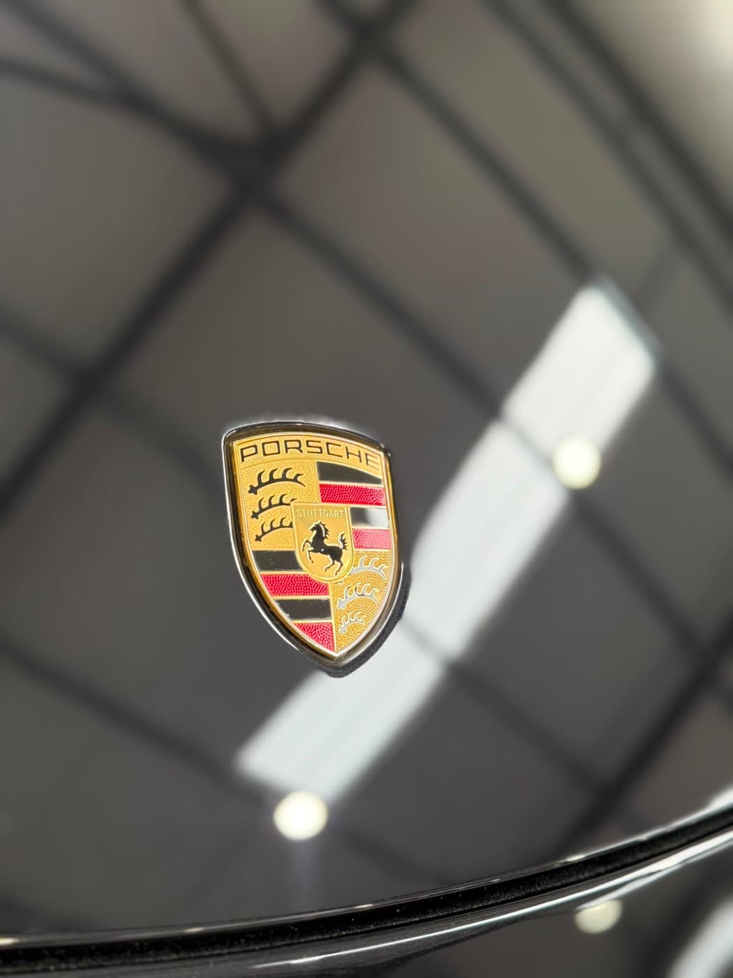 Close-up of a polished Porsche crest on glossy black paint